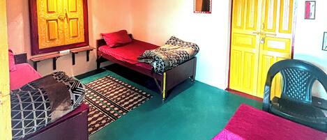 Habitación con dos camas, una silla y una mesita. Se observa una puerta y un espejo en la pared.