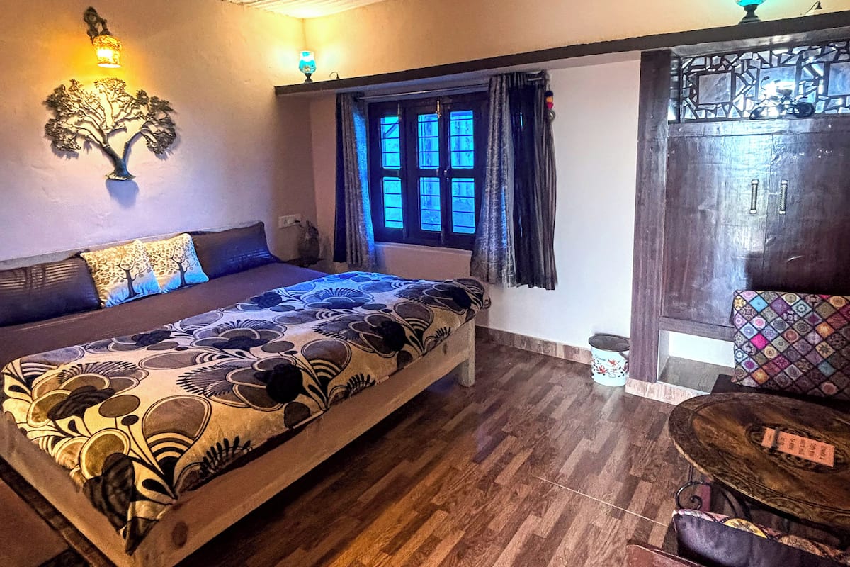A bedroom with a bed, a nightstand, a window with curtains, a wall-mounted lamp, and a decorative wall piece.