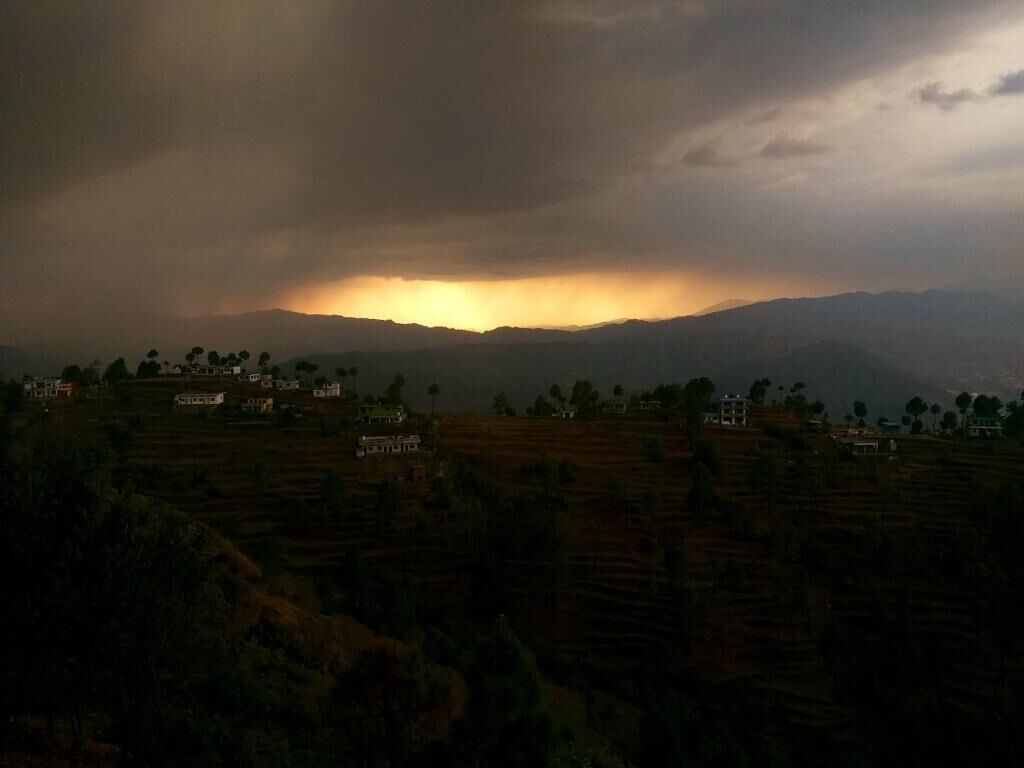 A rural landscape with terraced fields and scattered houses under a cloudy sky.