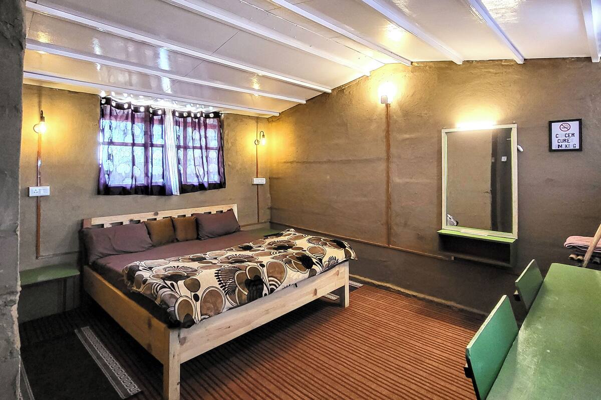 A bedroom with a bed, a mirror, a green table, and a window with curtains.