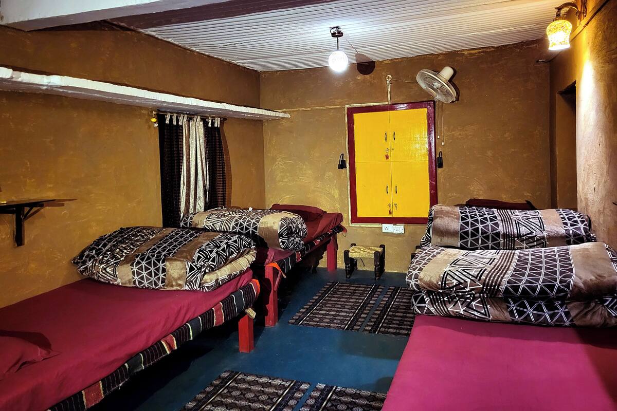 A room with two beds, a yellow wardrobe, a ceiling fan, and a wall-mounted light fixture.