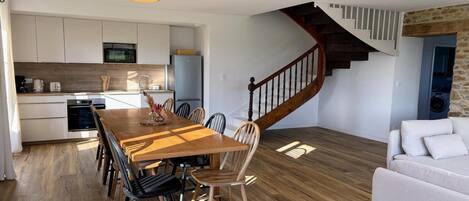 A modern kitchen with white cabinets, a wooden dining table, and a staircase with a wooden railing.