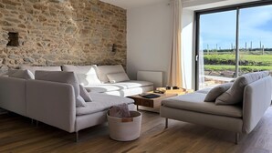 Ein modernes Wohnzimmer mit Steinwand, einem großen Fenster mit Blick auf die Landschaft und einem beigefarbenen Sofagarnitur.