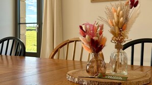Ein Esstisch mit zwei Glasvasen mit getrockneten Blumen, ein Holzstuhl und ein gerahmtes Bild an der Wand.