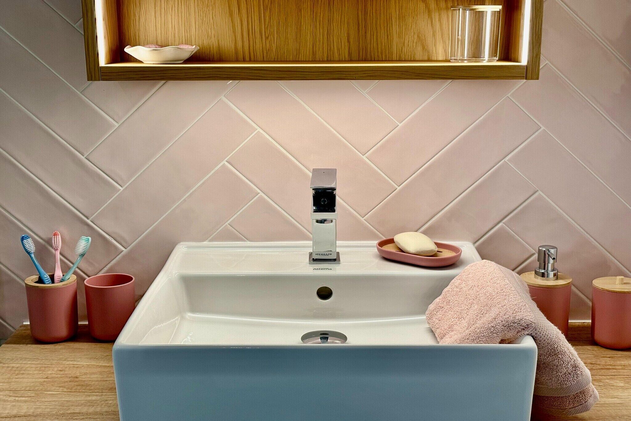 A bathroom with a white sink, a mirror above it, and a wooden shelf with a bowl and glasses.
