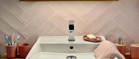 A bathroom with a white sink, a mirror above it, and a wooden shelf with a bowl and glasses.