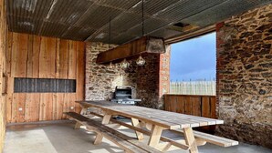 Ein rustikaler Essbereich im Freien mit einem langen Holztisch und Bänken, einer Steinsäule und Blick auf die Landschaft.
