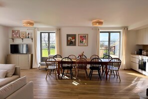 Un salon moderne comprenant un canapé, une table à manger avec des chaises, un téléviseur posé sur un meuble et des œuvres d’art accrochées aux murs.