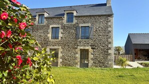A stone building with two windows and a door, surrounded by a well-maintained lawn and flowering bushes. - Lovely holiday cottage in Corseul (Corseul)