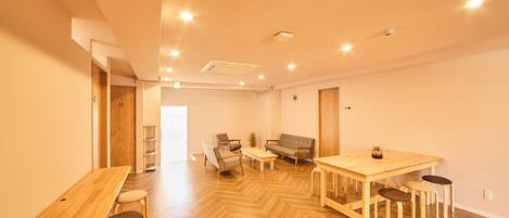 A spacious room with a wooden herringbone floor, a long table with chairs, a sofa, and a small potted plant.