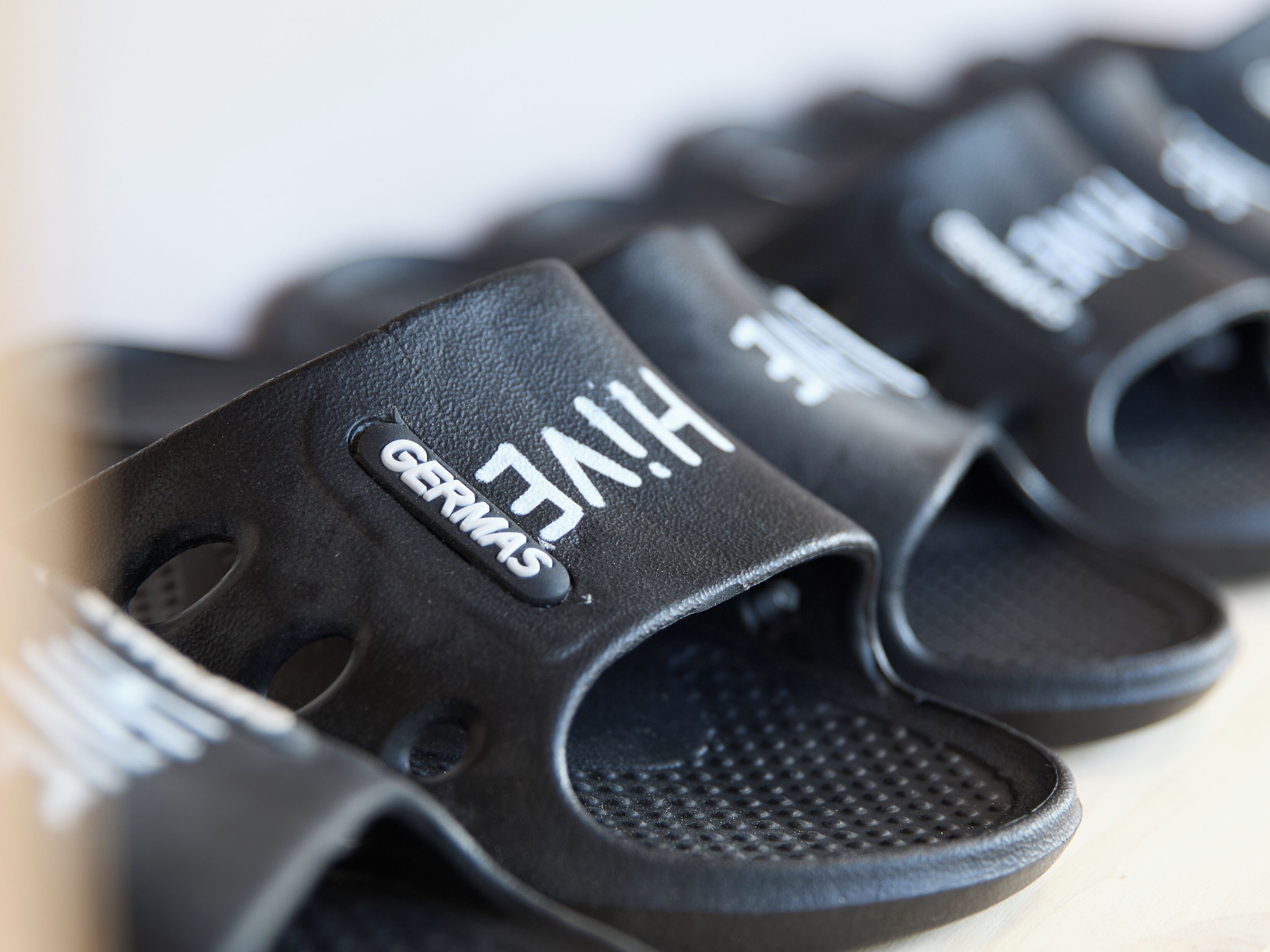 Primer plano de sandalias negras con el texto 'GERMAS' y 'VIH'.