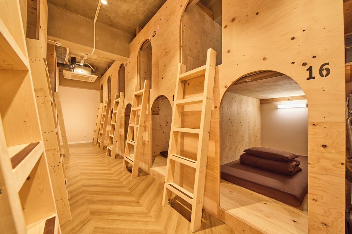 Une rangée de lits superposés en bois, dotés de compartiments numérotés, d’échelles en bois et d’un plancher à motifs en chevrons.