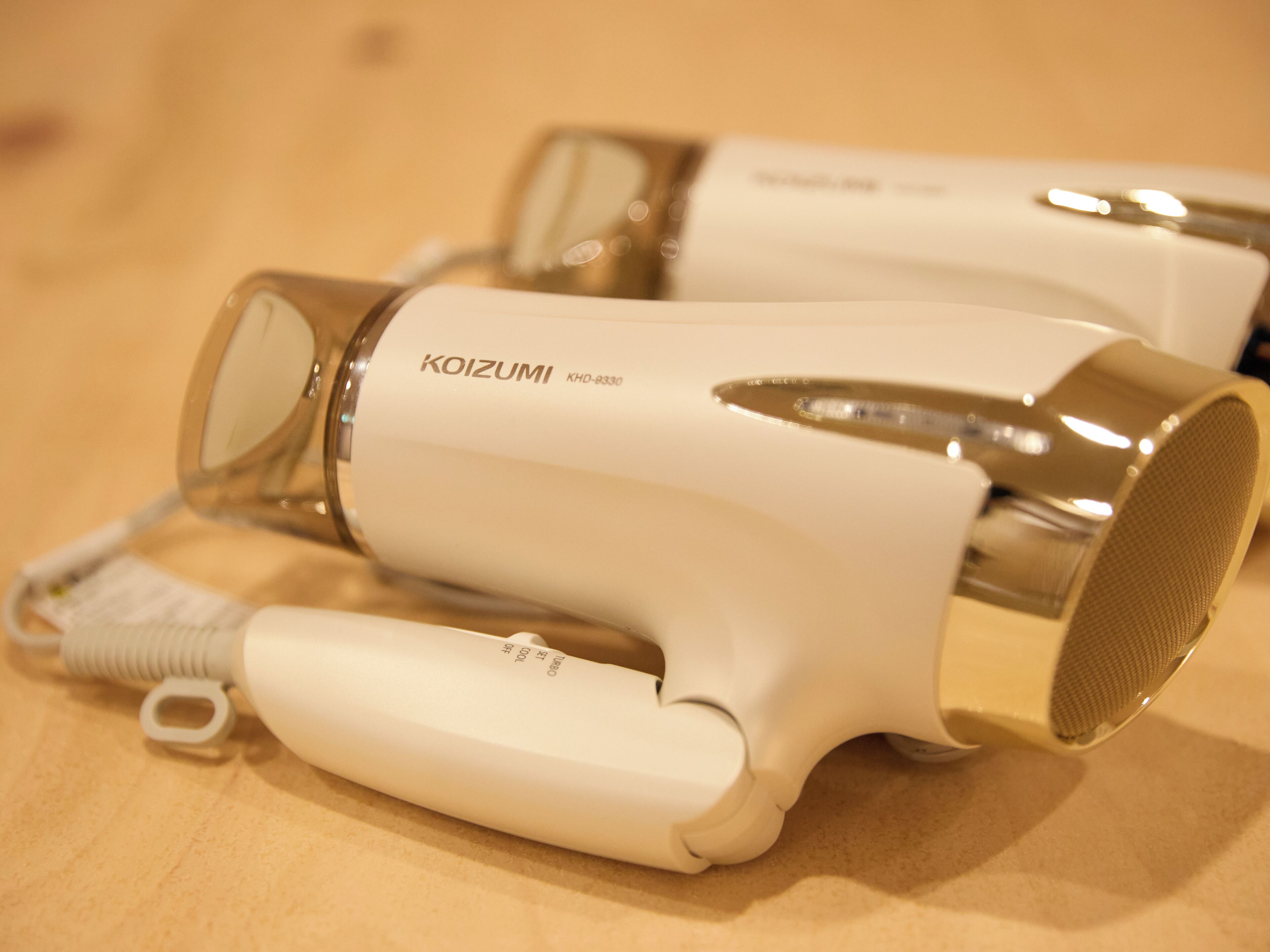 A white hairdryer with a metallic nozzle and a cord.