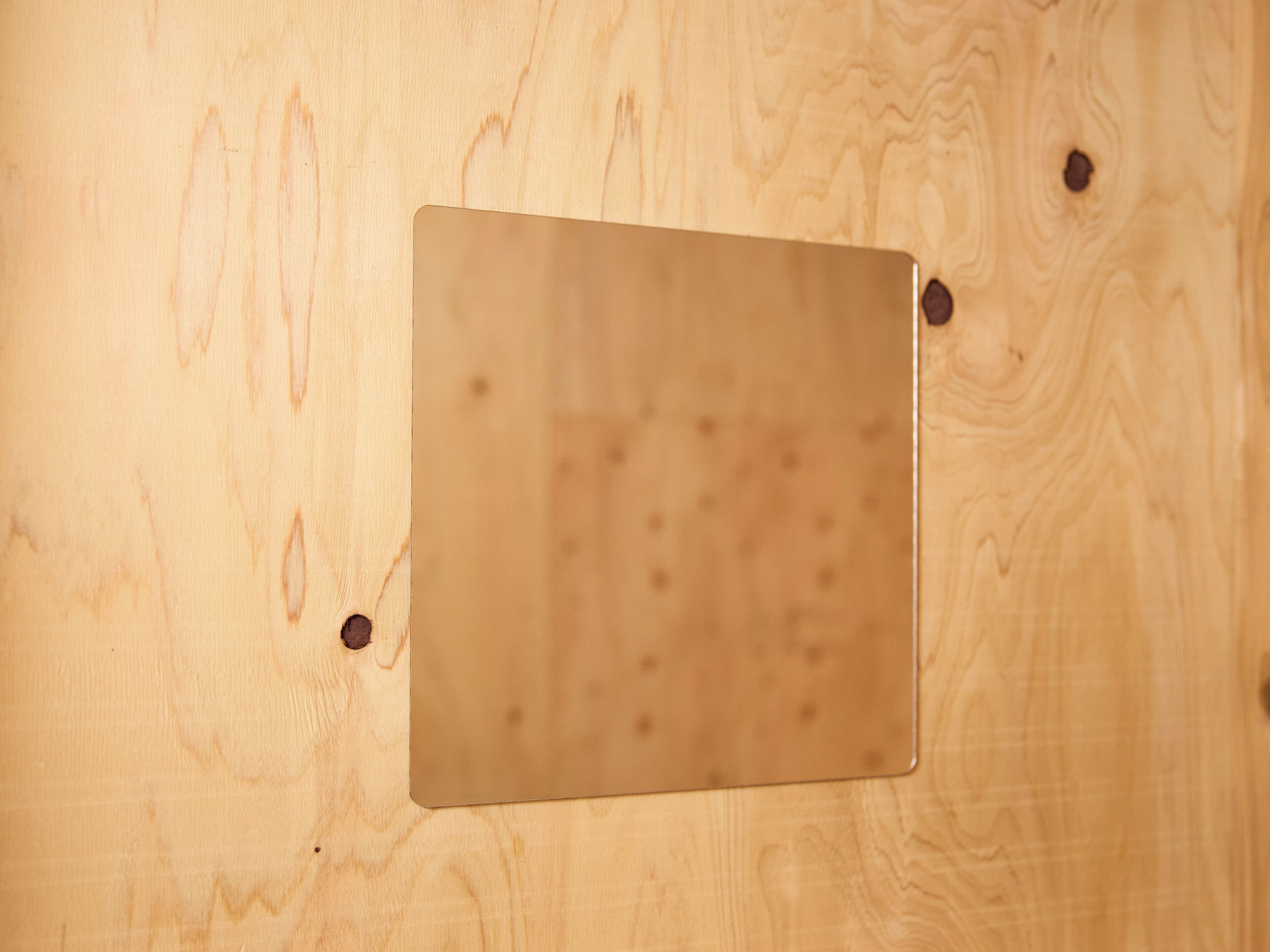 A wooden surface with a square, metallic object attached by four screws.