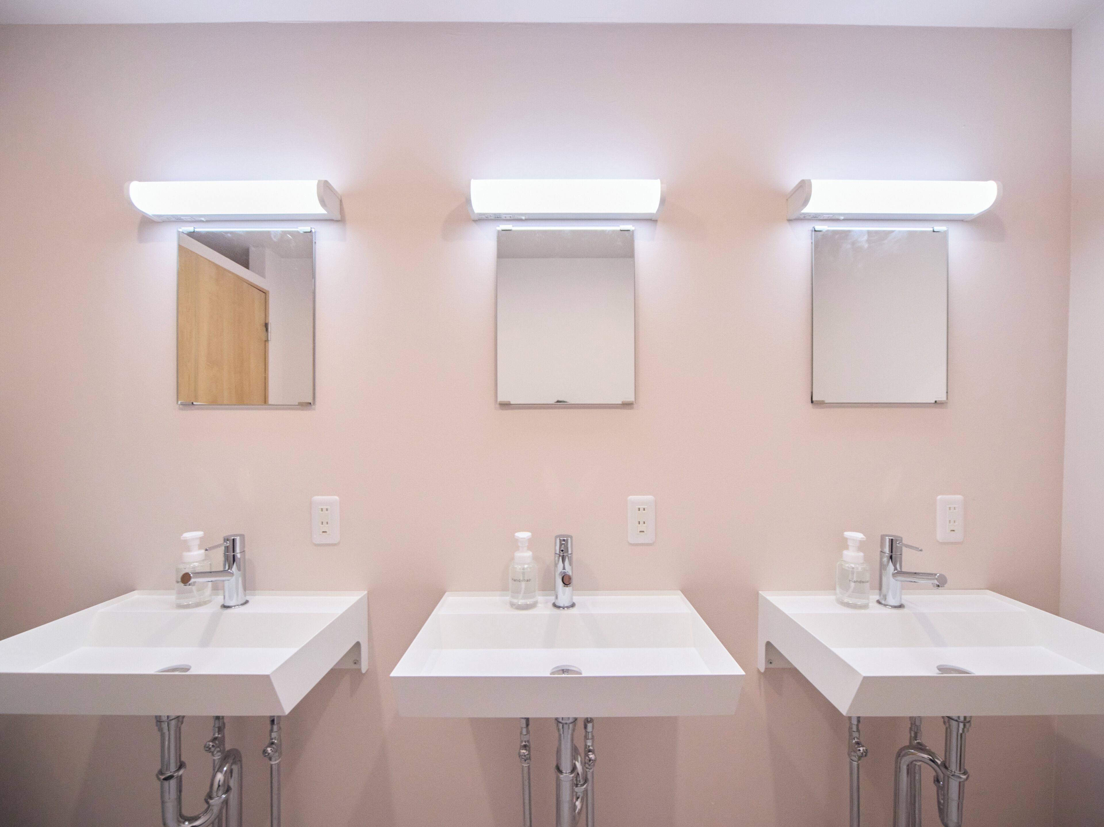 Three white sinks with mirrors above them, each with a light above.