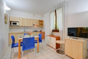 A compact kitchen with a microwave, stove, and dining area with blue chairs. - Studio in Porlezza am Luganersee (Porlezza)
