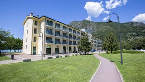 Um hotel de vários andares com fachada amarela, um caminho pavimentado e montanhas ao fundo.