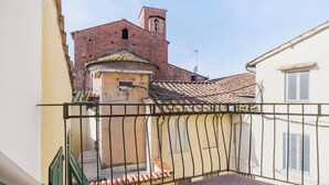 Ein Balkon mit Metallgeländer, Fliesenboden und Blick auf ein Gebäude mit einem Glockenturm.