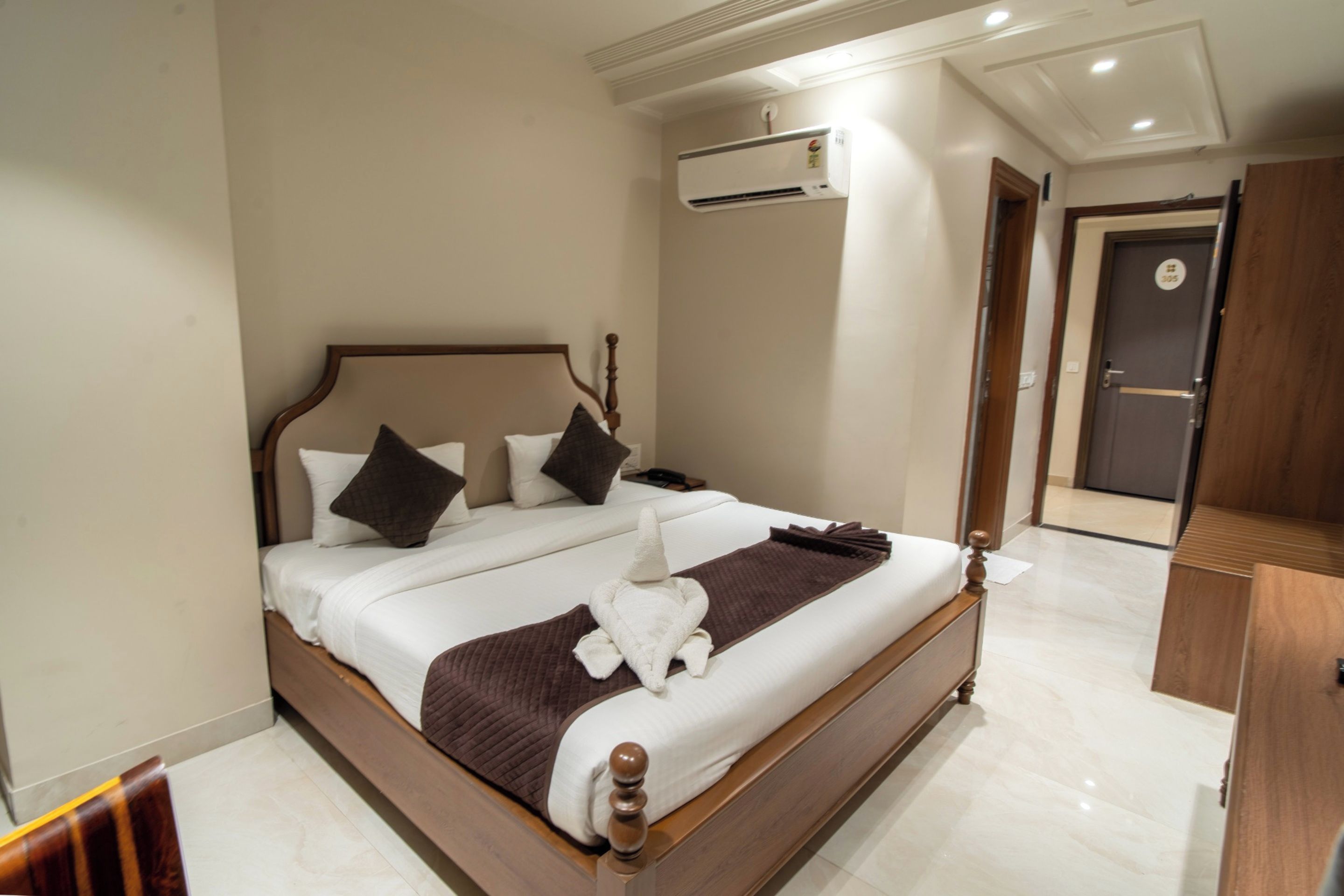 A hotel room with a large bed, a bedside table, an air conditioning unit, and a door with a number.