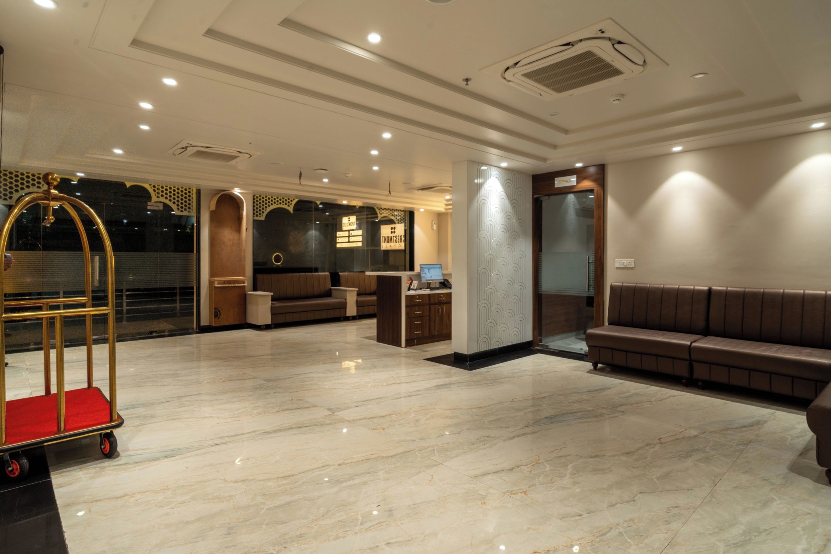 A hotel lobby with a reception desk, seating area, and a luggage cart.