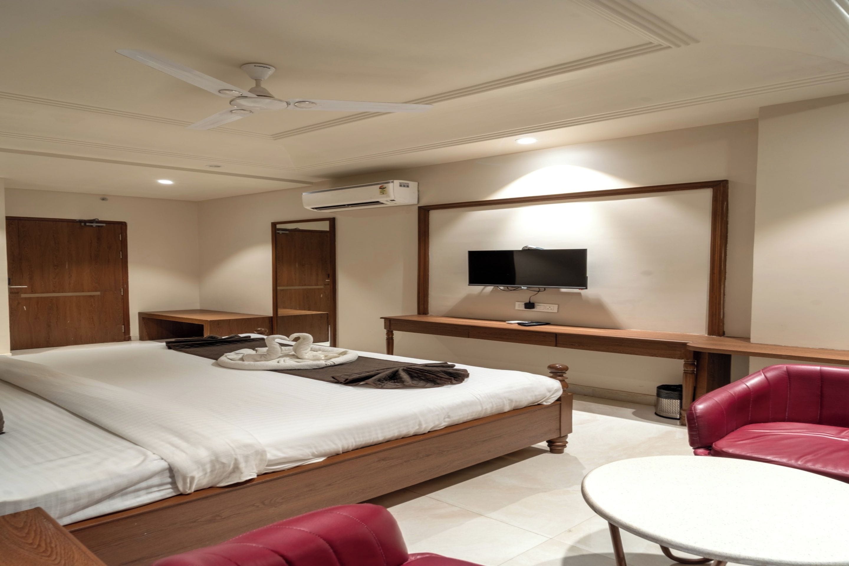 A hotel room with a bed, a desk with a flat-screen TV, a chair, and a ceiling fan.