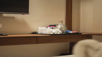 Een hotel bureau met een flatscreen televisie aan de muur, een dienblad met toiletartikelen, een fles en wat snacks.