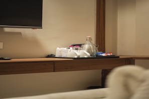 A hotel desk with a flat-screen TV mounted on the wall, a tray with toiletries, a bottle, and some snacks.