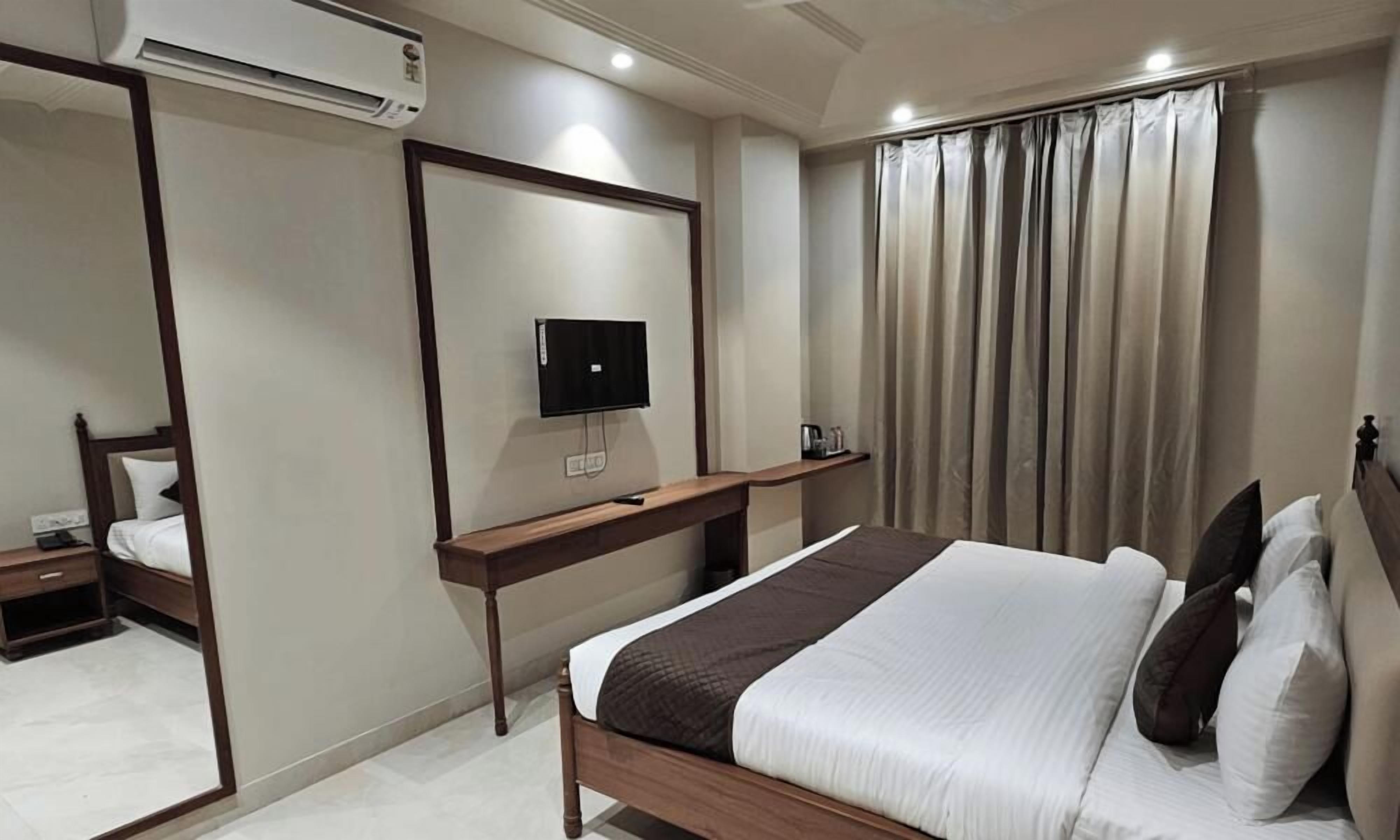 A hotel room with a bed, a television mounted on the wall, a bedside table, and a window with curtains.