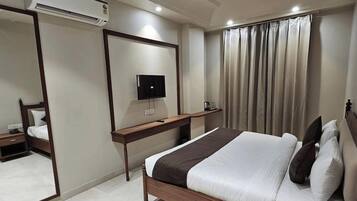 A hotel room with a bed, a television mounted on the wall, a bedside table, and a window with curtains.