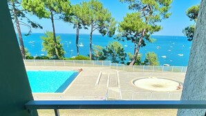 Piscina con vistas al mar y barcos, rodeada de árboles.