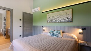 Una cama bien hecha con cubrecama acolchada, aire acondicionado montado en la pared, un cuadro floral enmarco y una lámpara de noche.