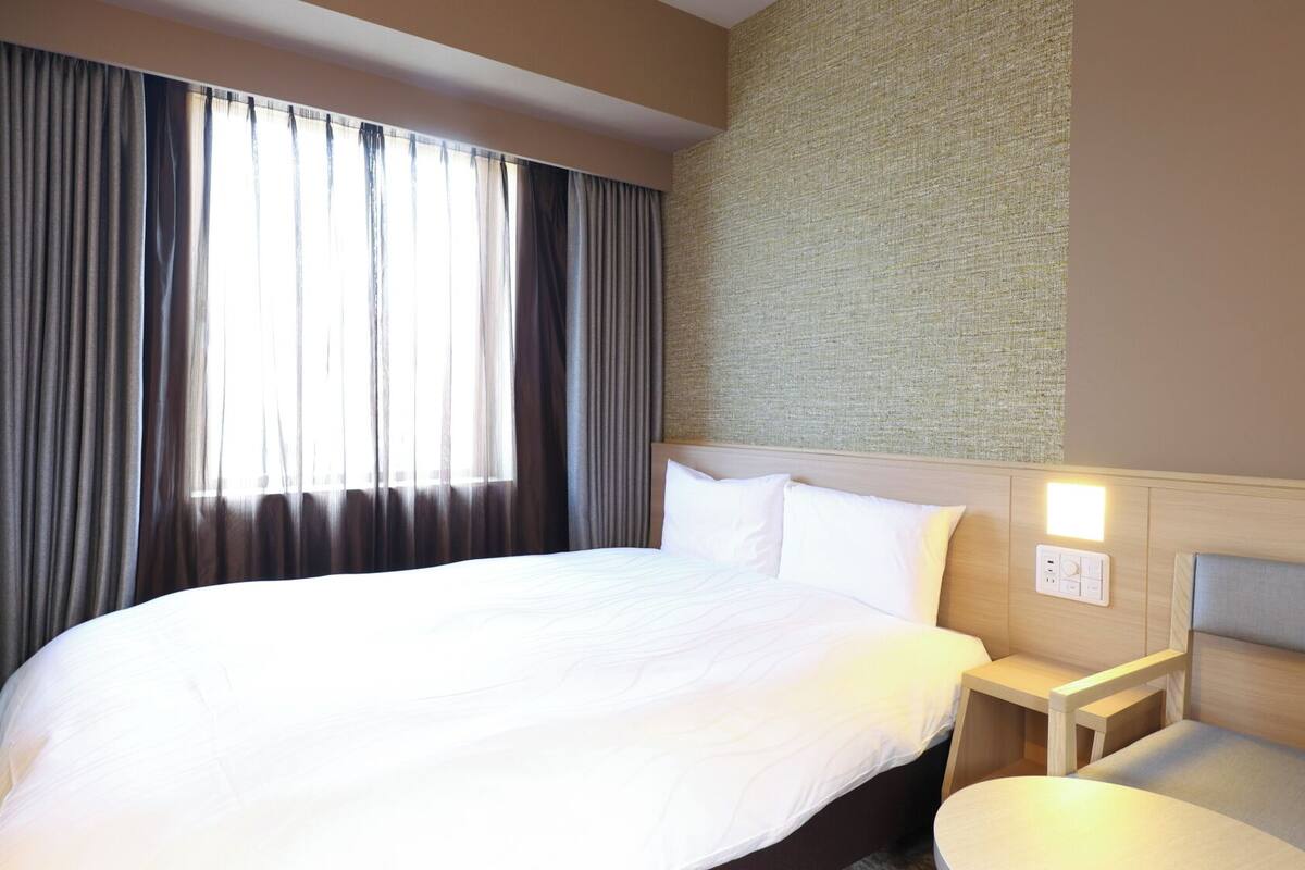 Una habitación de hotel con una cama grande, una mesita de noche, una pequeña mesa redonda y una lámpara fijada a la pared.
