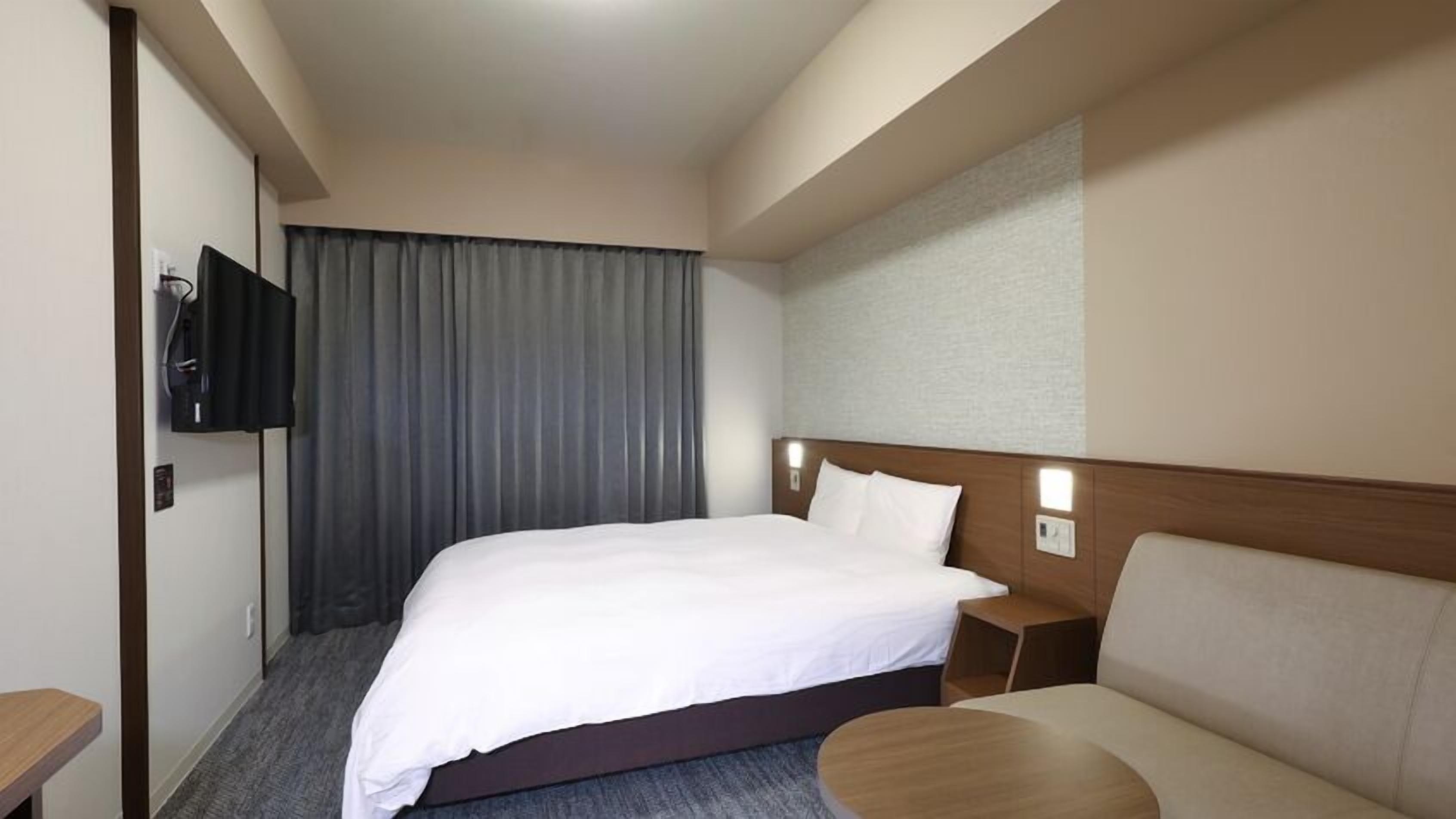 Een hotelkamer met een bed, een televisie aan de muur, een bank en een klein tafeltje.