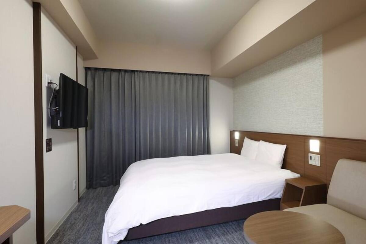 Una habitación de hotel con una cama, un televisor montado en la pared, un sofá y una pequeña mesa.