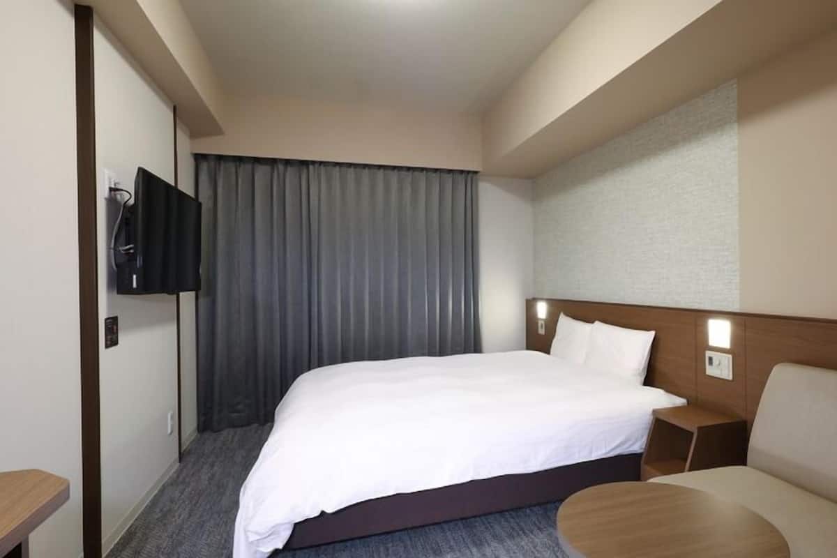 A hotel room with a bed, a TV mounted on the wall, a sofa, and a small table.