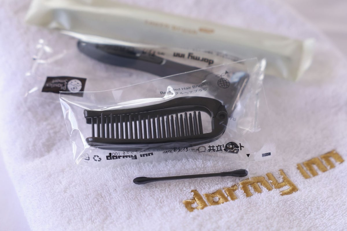 A package containing a hairbrush and a comb, placed on a white towel with the text "darmy inn" embroidered on it.