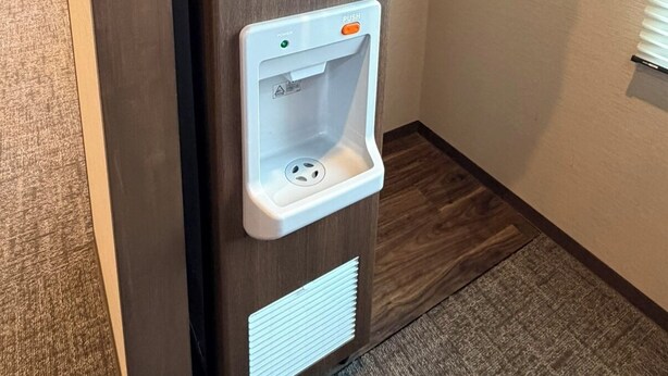 A wall-mounted water dispenser with a push button and a cup holder. - Dormy Inn Tsuruga (TSURUGA SHI)