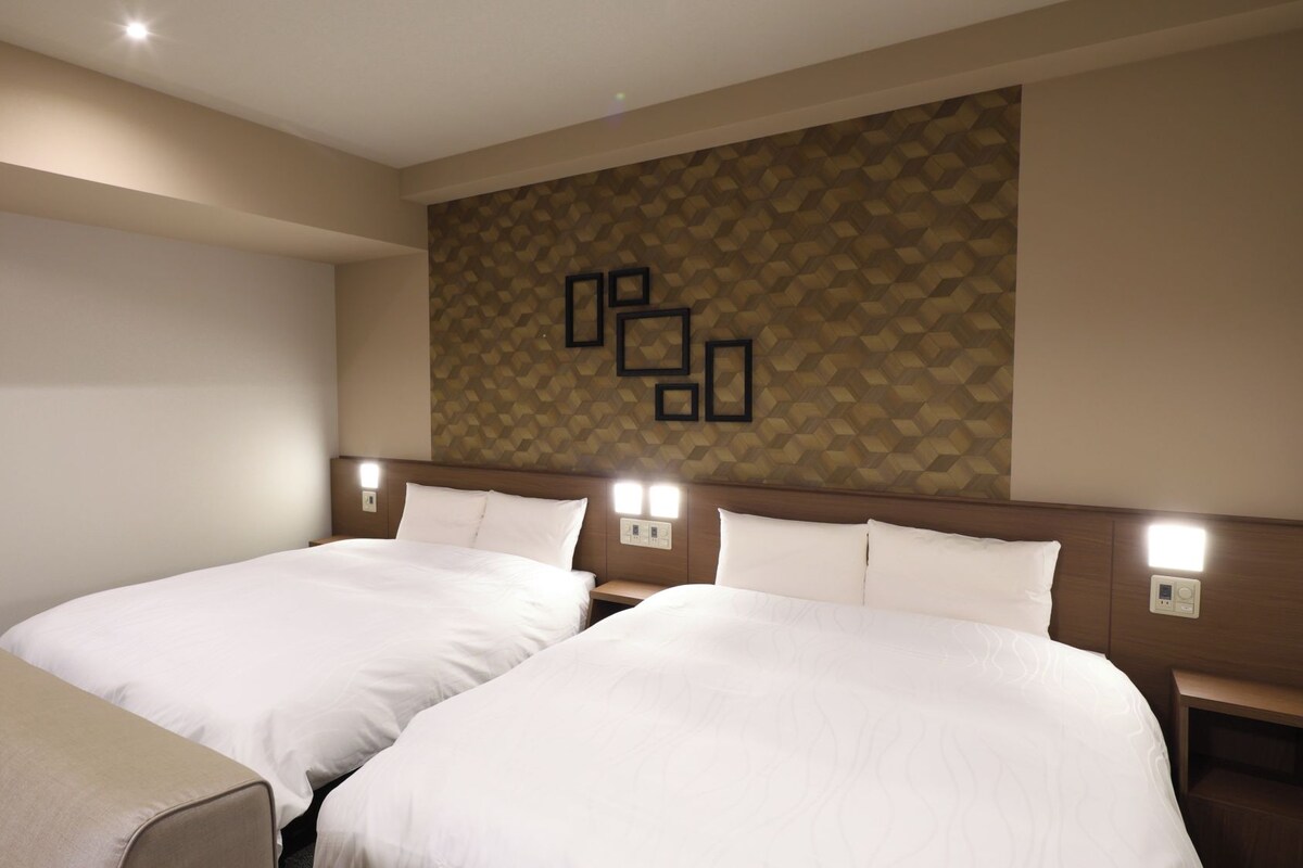 A hotel room with two beds, a bench, and a wall with geometric patterned wallpaper.