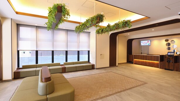 A hotel lobby with a reception desk, seating area, and large windows with blinds. - Dormy Inn Tsuruga (TSURUGA SHI)