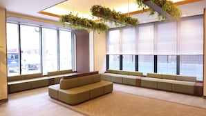 A modern waiting area with seating, large windows, and hanging plants. - Dormy Inn Tsuruga (TSURUGA SHI)