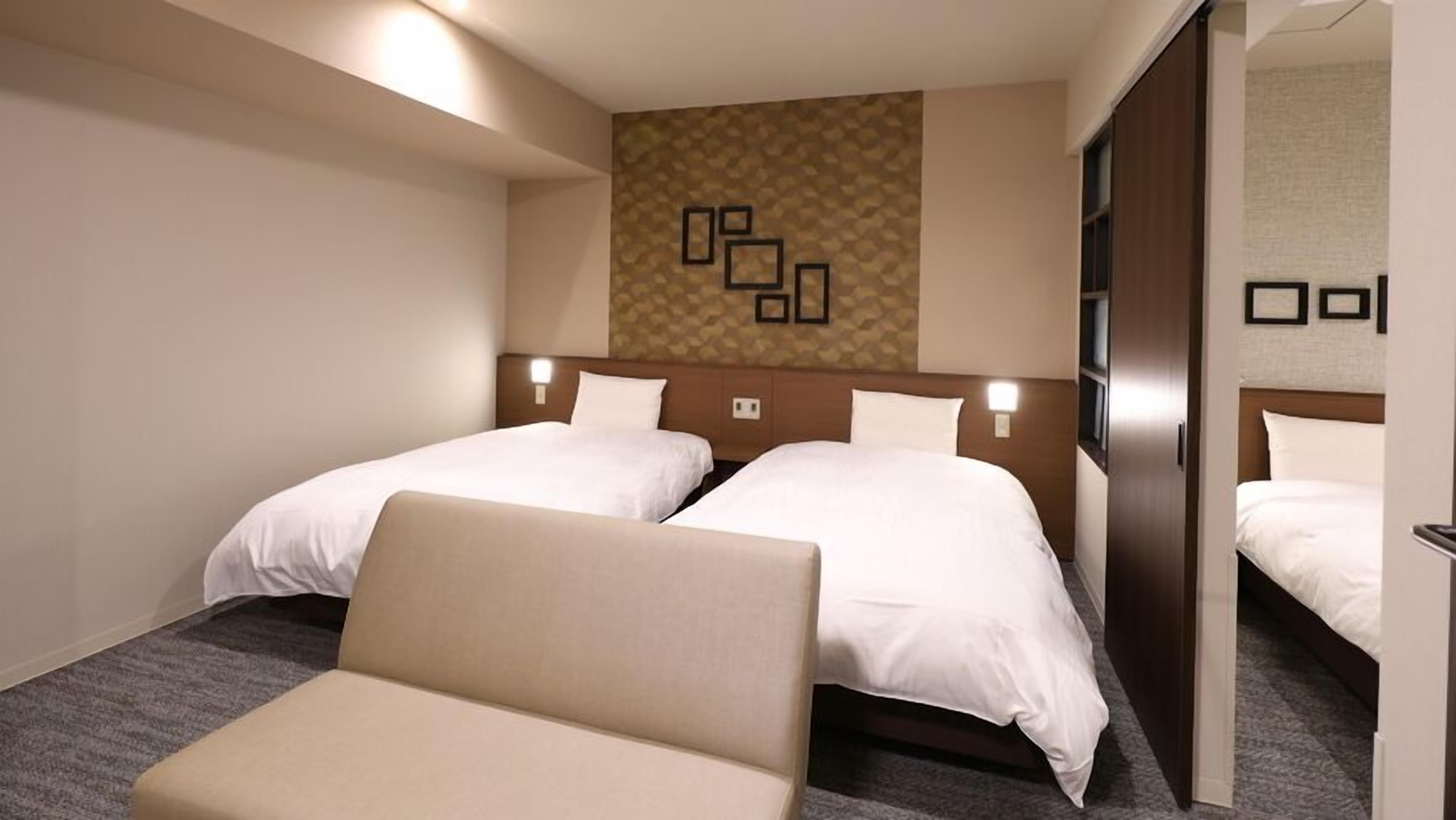 Een hotelkamer met twee bedden, een bank, een behangetapijt en een spiegel.