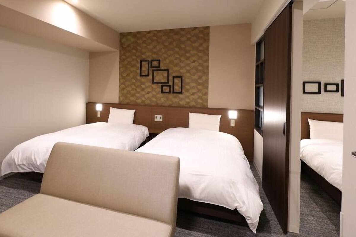 Habitación de hotel con dos camas, un sofá, un papel tapiz estampado y un espejo.