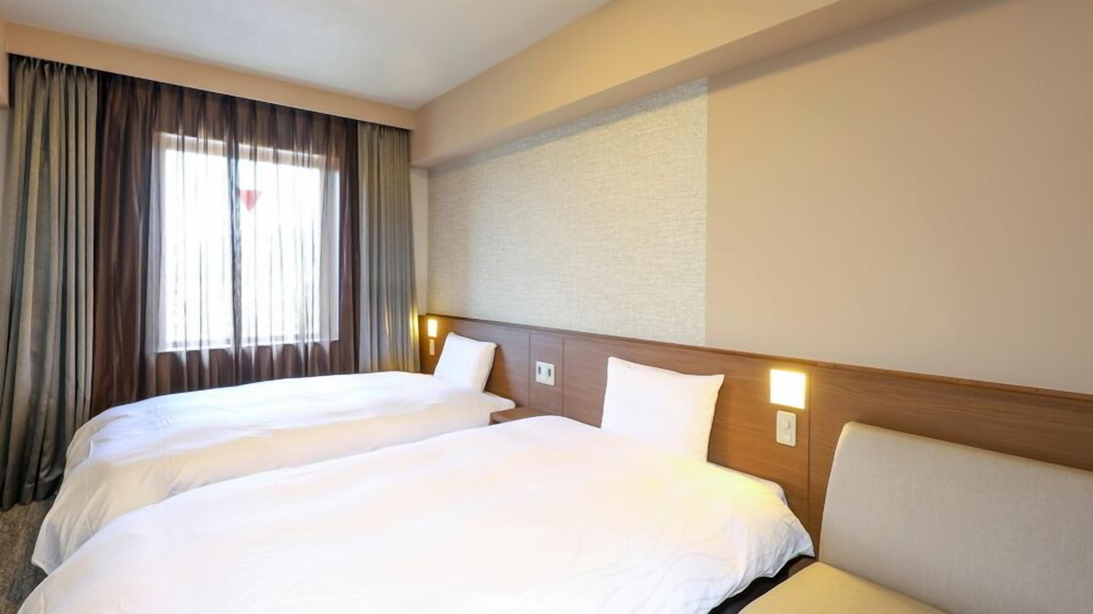 Een hotelkamer met twee bedden, een groot raam met gordijnen en een wandlamp.