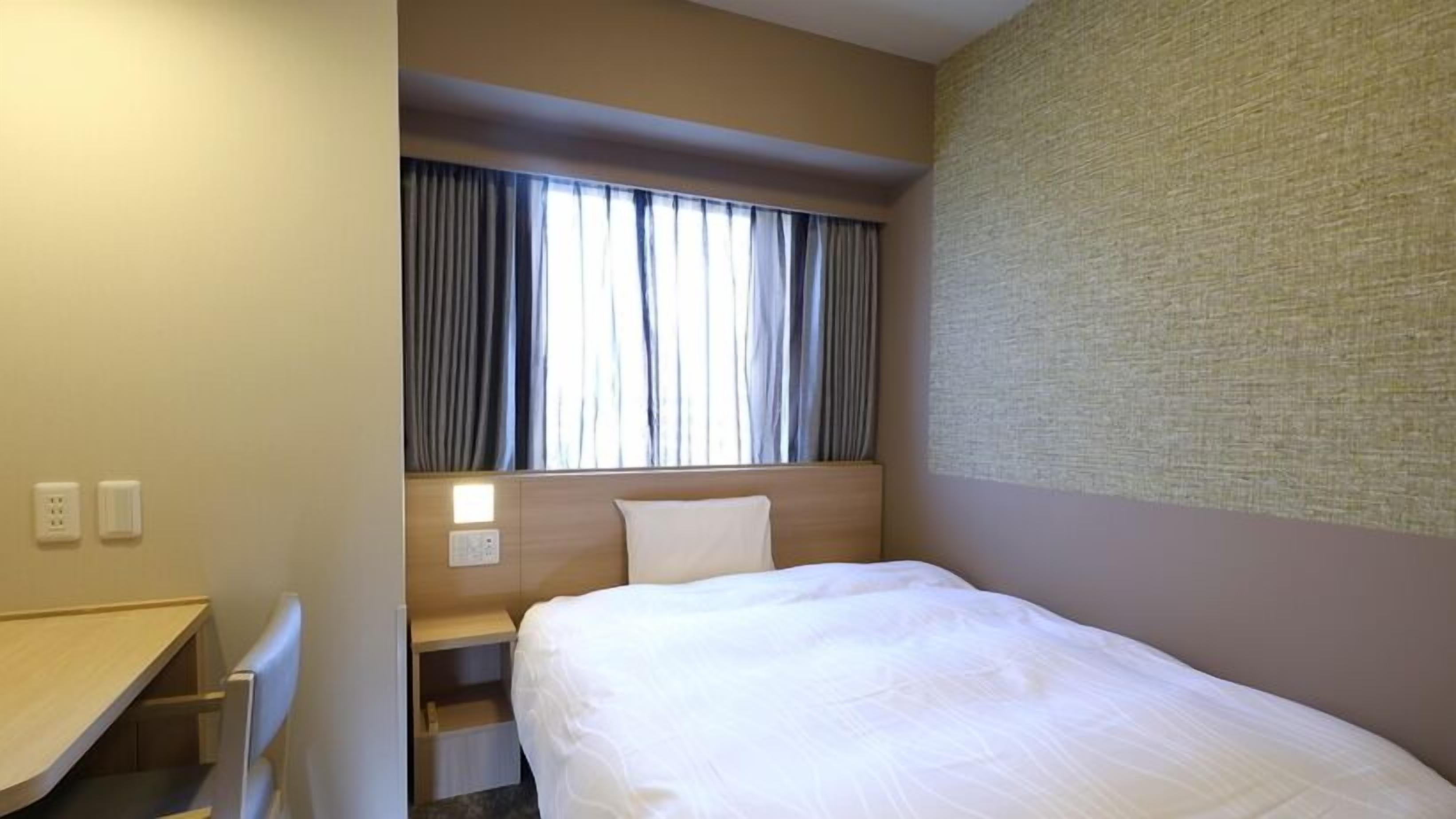 Hotelkamer met een bed, bureau, nachtkastje, raam met gordijnen en een structuurwand.