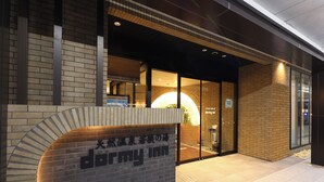 A hotel entrance with a brick facade, a glass door, and a sign with Japanese characters. - Dormy Inn Tsuruga (TSURUGA SHI)