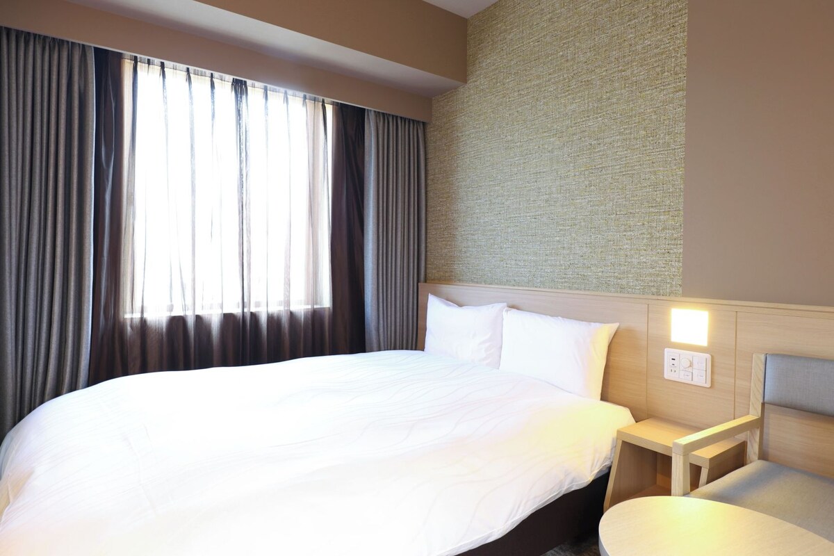 A hotel room with a large bed, a bedside table, a small round table, and a wall-mounted light.