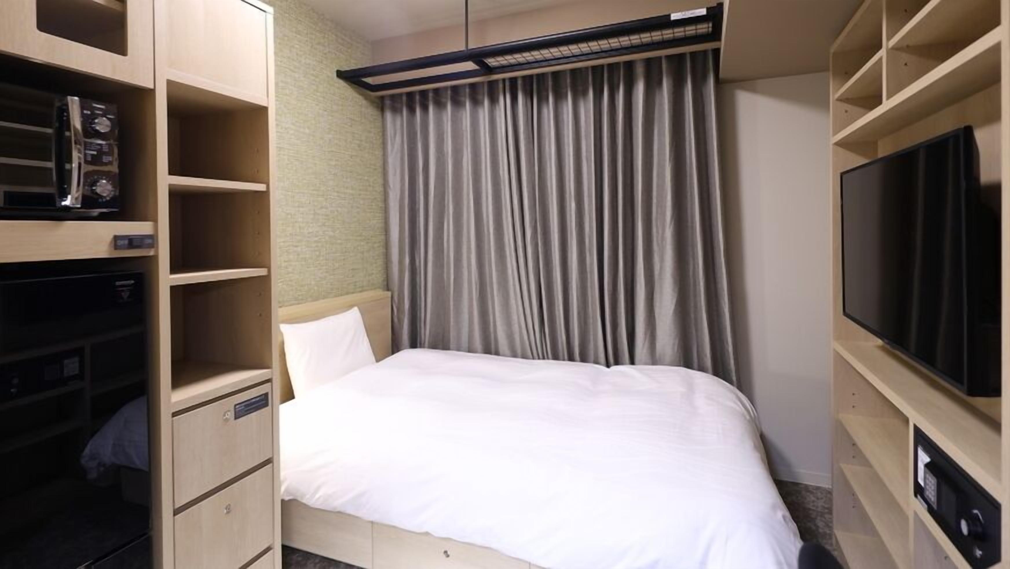 Een hotelkamer met een bed, een televisie, inbouwopbergruimte en een gordijn.