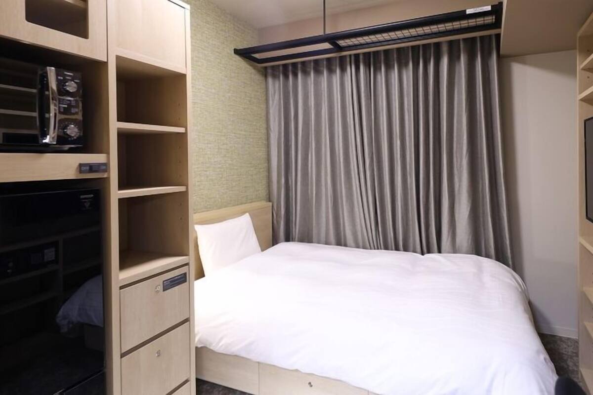 Una habitación de hotel con cama, televisión, almacenamiento integrado y cortina.