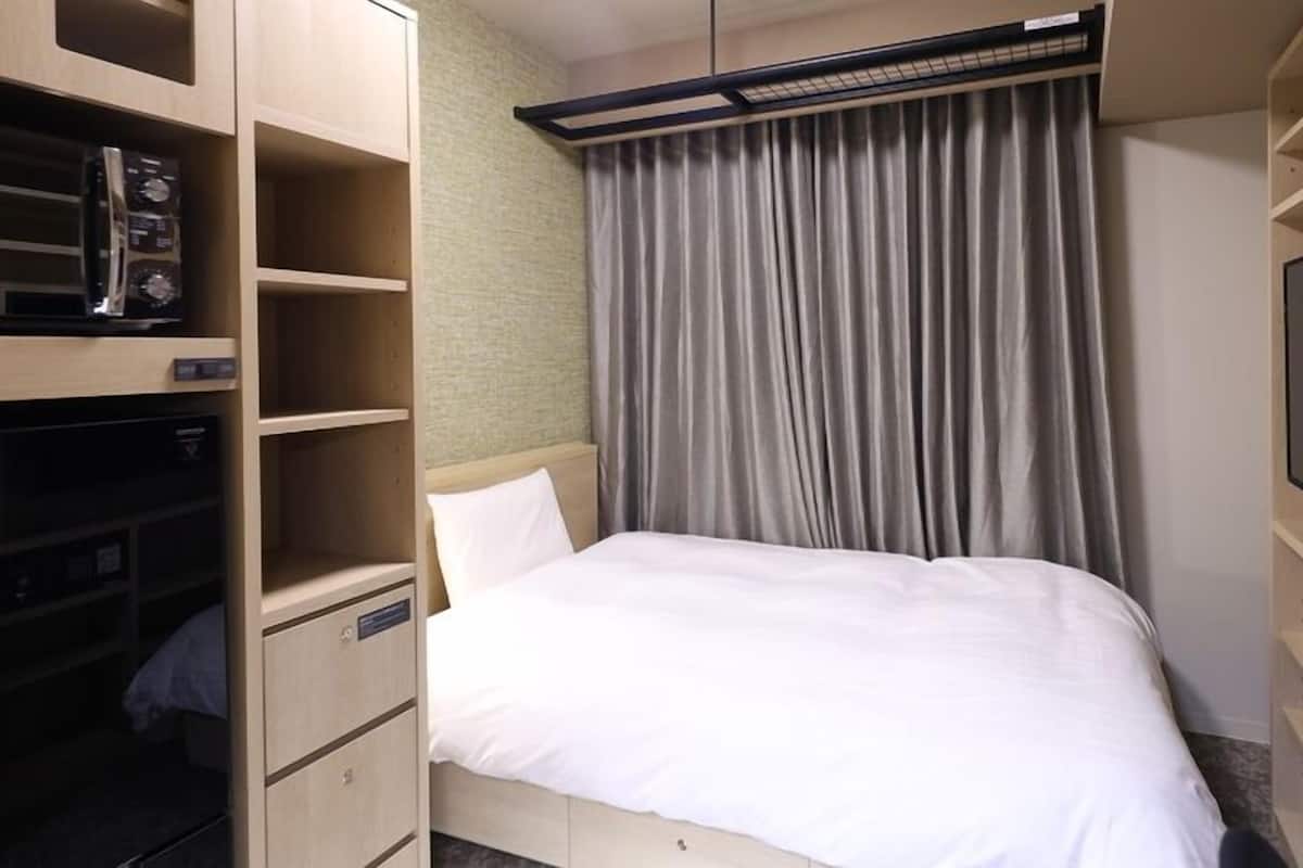 A hotel room with a bed, a TV, built-in storage, and a curtain.