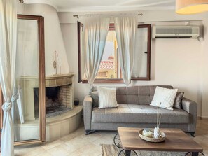 Ein Wohnzimmer mit Kamin, einer Couch, einem Couchtisch und Blick auf ein Gebäude mit orangen Dächern.
